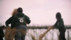 Rack focus from grass blades to volunteers picking up trash on beach Stock Footage