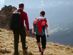 Wing suit fliers/ hikers ascend through mountain meadow Stock Footage