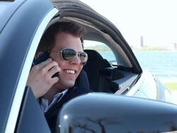 MS young man sitting in his modern car smiling and talking on his cell phone on sunny day near a lake / Minneapolis, Minnesota, United States Stock Footage