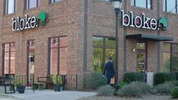 Small business owner arrives at brick storefront, unlocks door to clothing shop, and enters Stock Footage