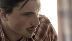 Young man broods on motel bed as young woman paces in background Stock Footage