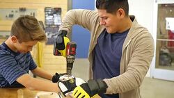 Mid adult Hispanic man teaches Hispanic preteen boy how to drill a hole in board Stock Footage