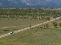 Aerial SUV pulling camper on Route 89/ zoom out traffic on road with Grand Tetons/ Wyoming Stock Footage