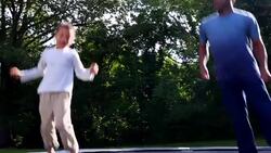 MS LA Smiling father and young son jumping on trampoline in backyard on summer morning Stock Footage