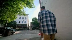 Young man carrying skateboard steps out of alley onto downtown sidewalk Stock Footage
