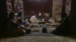 Virgin Mary sitting holding baby Jesus with Joseph and three wise men sitting nearby with stone walls and straw on floor Stock Footage