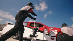 Pit-crew jacks race-car and removes lug-nuts, man runs with tire Stock Footage