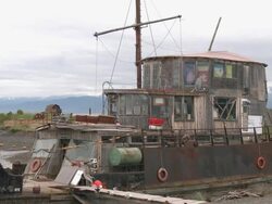 "CU of three tiered wooden cabin of run down and rusted metal fishing boat dry-docked at Homer boat harbor on Homer Spit, other boats also dry-docked, snow capped mountains of Kachemak Bay State Park and Wilderness Park in background." Stock Footage