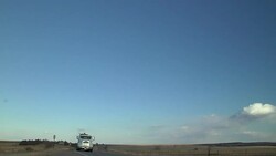 Semi truck carries a backhoe on a trailer and drives down a rural highway and passes a farm tractor discing a field. Stock Footage