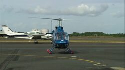 An airplane passes behind a helicopter with its rotor blades spinning. Stock Footage