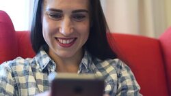 smiley woman sitting on red chair and using her smartphone at home Stock Footage