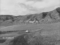 1950: DENVER, COLORADO: SUMMER ATTRACTION: WS Late model sedan driving on road toward Rocky Mountain foothills. PAN Down seating of Red Rocks amphitheatre, two men walking on stage. Instructional Video