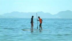 Brazilian boy shakes girl off paddleboard, loses balance and falls into the water off Copacabana Beach Stock Footage