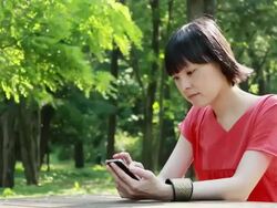 MS Shot of young woman using smartphone in park / Nakano, Tokyo, Japan Stock Footage