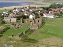 Aerial long shot view of ruins of monastery and coastline of Holy Island / zoom in monastery / England Stock Footage