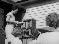 B/W 1934 woman standing in bookmobile on street looking at book / children in foreground / newsreel Stock Footage