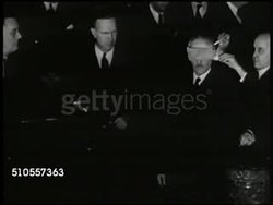 1940: U.S. PEACETIME DRAFT: CU Newspaper 'FDR Orders Draft Oct 16.' INT VS Secretary of War Henry L. Stimson (1867-1950) blind folded picking lottery. HA WS Audience. HA WS President Franklin Roosevelt at podium 'first number is... 158.' WWII Instructional Video