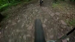 The front wheel of a bicycle follows another cyclist down a rocky mountain path. Stock Footage