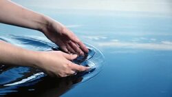 A woman uses her hands to create ripples in water refelcted in a blue sky.  Stock Footage