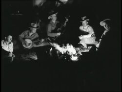 Cowboys play banjos around a campfire. News Clip