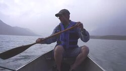 Man paddles boat on mountain lake, in rainstorm Stock Footage