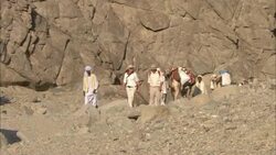 A caravan walks across rocky terrain next to a mountain. Stock Footage