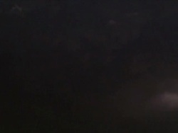 Shot of clouds being illuminated by lightning within the thunderstorm, camera tips down to reveal storm above ground. At end of shot very bright forked lightning strikes ground under the storm. Stock Footage