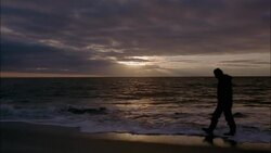 A man walks along the beach as water washes up on his feet in Sylt, Schleswig-Holstein, Germany. Stock Footage