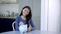 Woman day dreaming and putting coins in piggy bank Stock Footage