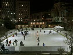 Busy outdoor ice skating rink in city surrounded by tall buildings at night Stock Footage