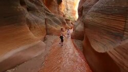Follow young hiker boy and young hiker girl down riverbed through canyon narrows Stock Footage