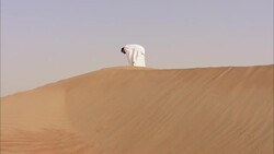 A man gestures as he prays on a sand dune. Stock Footage