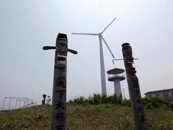 MS View of Cheonhadaejanggun (Wooden Statue of Great General Under Heaven) and Jihayeojanggun (Wooden Statue of Female General Under Ground) with wind power plant / Jeju-do, South Korea Stock Footage