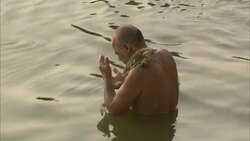 A devotee sitting on a ghat by the Ganges rubs water on his shaved head. Stock Footage