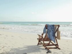 Deck chair on sandy beach at water's edge Stock Footage