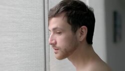 Young man stares out bedroom window and drinks coffee Stock Footage