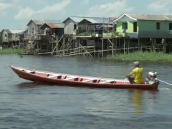 brazilian man riding his motorboat over the river with palafitte houses at background Stock Footage