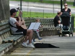 A Man playing the guitar on a park bench in Central Park.  Two little children come over to watch. Stock Footage