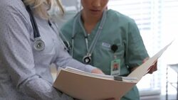 Doctor and nurse discussing medical record in examination room Stock Footage