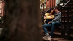 New York couple in love laugh and nuzzle on stoop of brownstone apartment, people cross in foreground (dolly-shot) Stock Footage