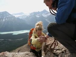Climber assists teammate while climbing rock above mtns Stock Footage