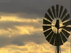 MCU Golden clouds reflecting sunset light panning right to silhouetted windmill turning Stock Footage