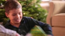Young boy tears off wrapping paper in a frenzy in front of Christmas tree Stock Footage