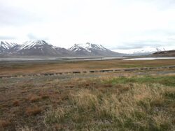 A man riding his bicycle on the road to Adventdalen in Longyearbyen, Svalbard with beautiful mountains covered by snow in the back Stock Footage