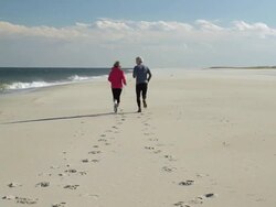 WS Mature couple jogging on beach side/ Sea Bright / New Jersey / USA Stock Footage