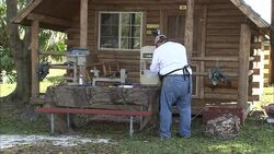 A craftsman uses woodworking equipment in front of a log cabin. Stock Footage