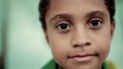 Young boy wrapped in Brazilian flag blinks and smiles at camera in soccer stadium Stock Footage