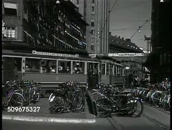 1943: STOCKHOLM, SWEDEN: STREET SCENES: HA WS Tram, light traffic & people walking, bicycling on bridge. Tram passing parked bicycles. Young females walking w/ bike past street vendor. WS Men in outdoor cafe w/ entertainment, MS Male w/ coffee cup. Instructional Video