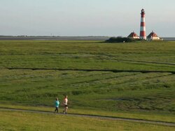 WS View of people walking on road through grass field near Westerhever lighthouse / Westerhever, Schleswig Holstein, Germany Stock Footage