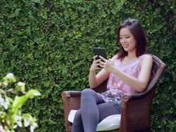 WS Chinese woman using digital tablet in garden with plants in foreground Stock Footage